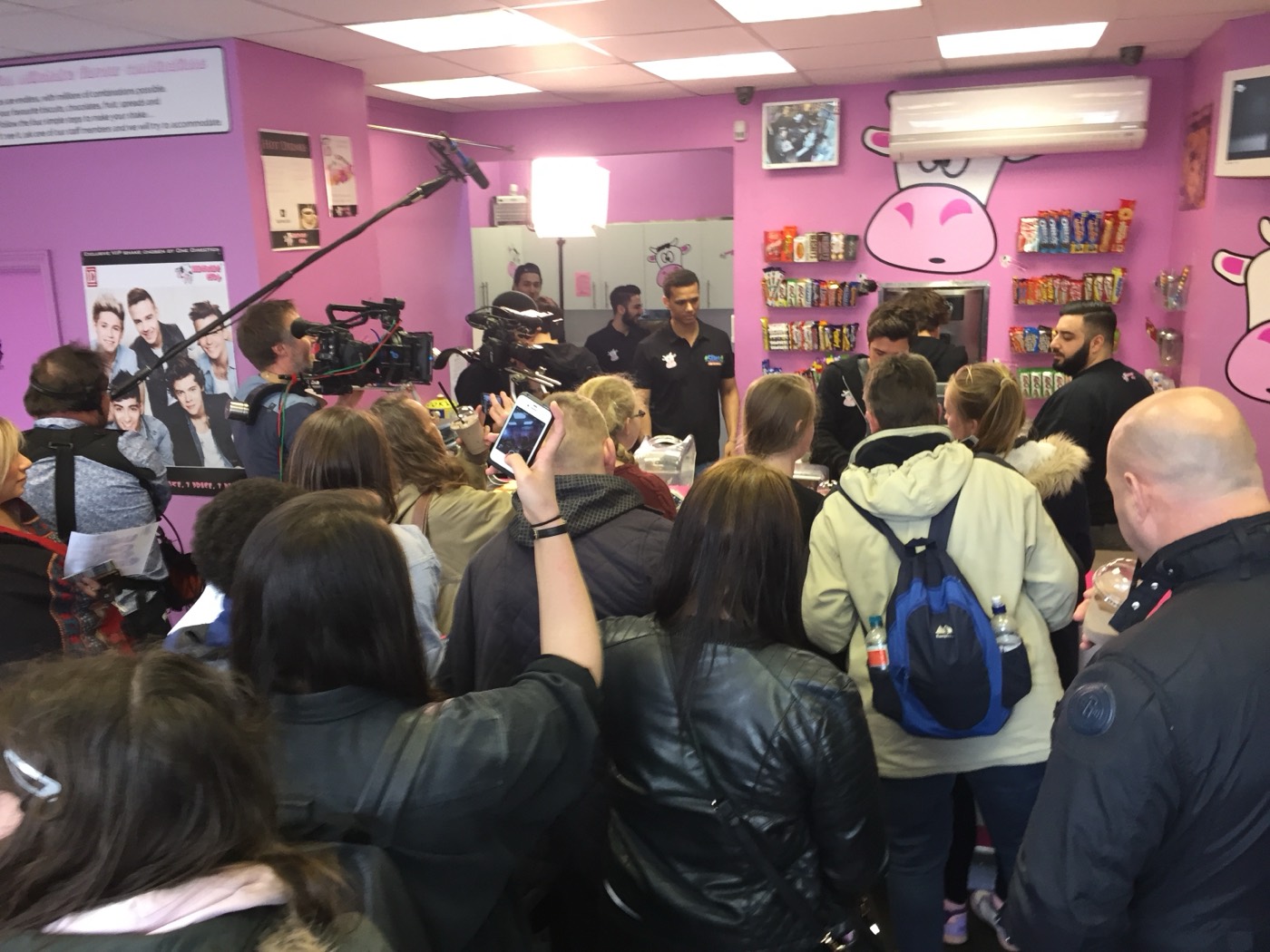 A camera crew and a crowd of people filling the pink interior of Milkshake City during a shoot