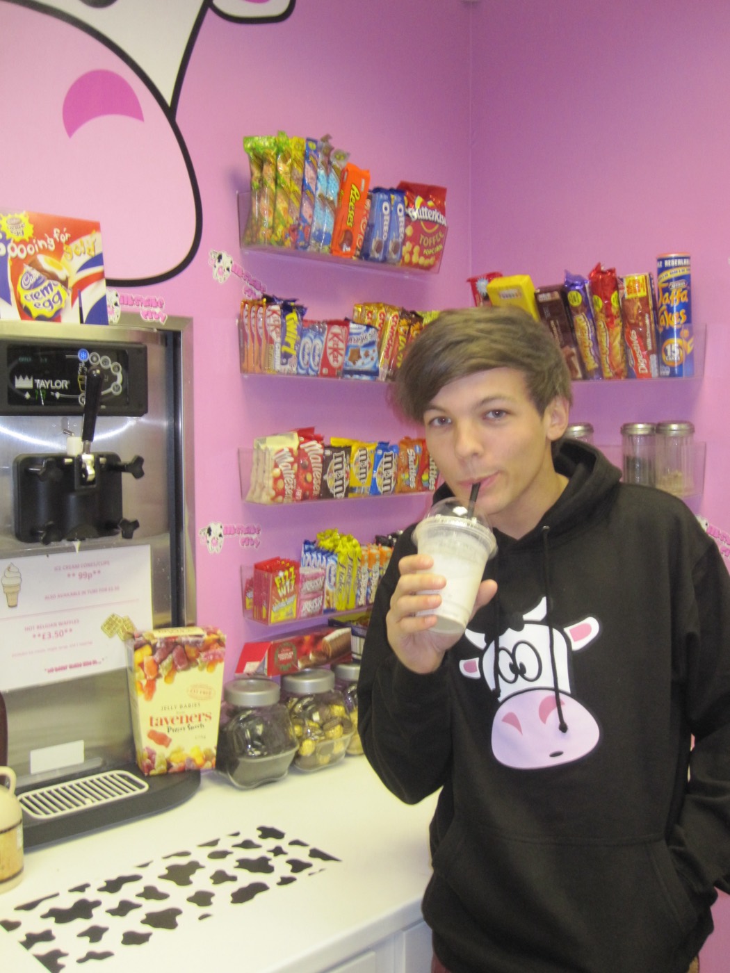 Louis Tomlinson drinking a milkshake in Milkshake City, wearing a Milkshake City cow-logo hoodie