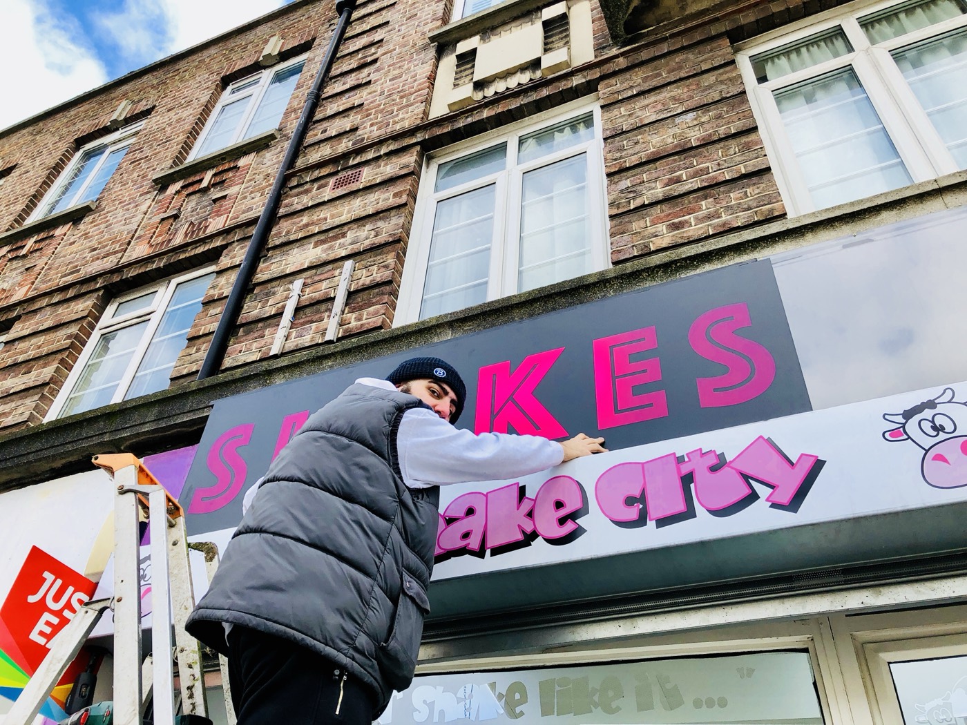 A man on a ladder removing the Milkshake City shopfront signage