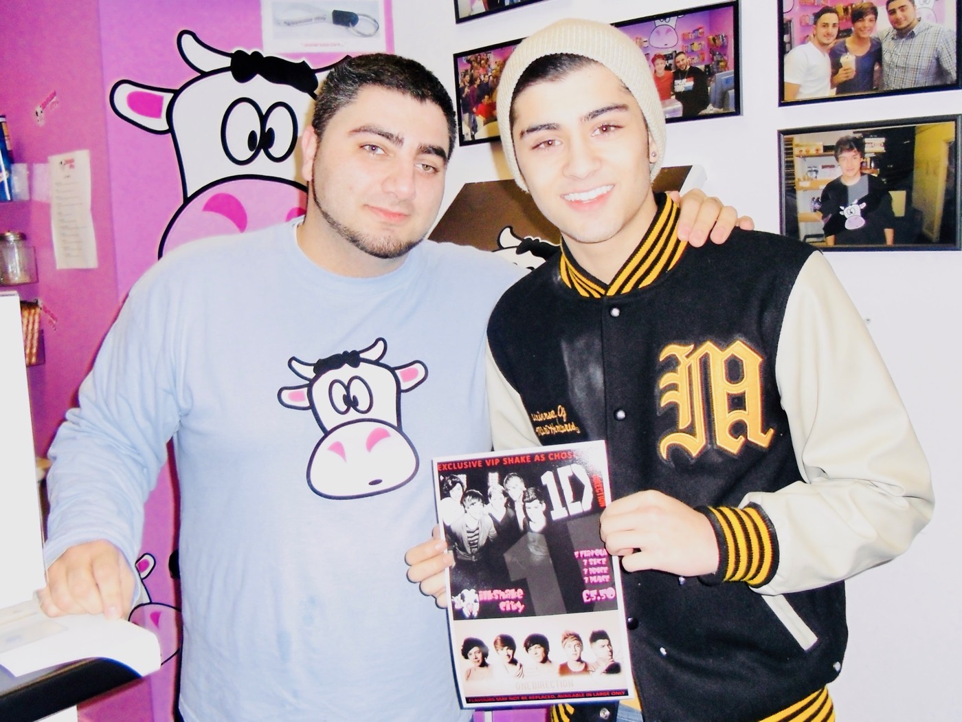 Zayn Malik holding a One Direction magazine in Milkshake City, beside a member of staff in a cow-logo top